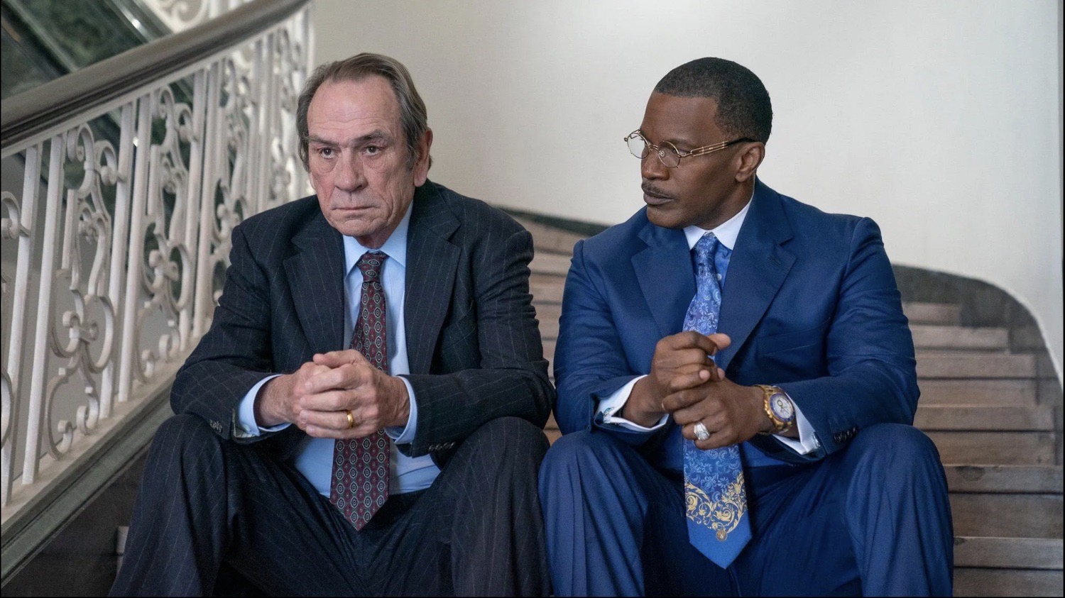 Jamie Foxx in a blue suit and Tommy Lee Jones in pinstripes seated on a staircase, The Burial