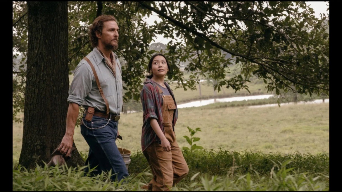 Matthew McConaughey and Angelina LookingGlass walking through an Oklahoma field in worn denim and layered workwear