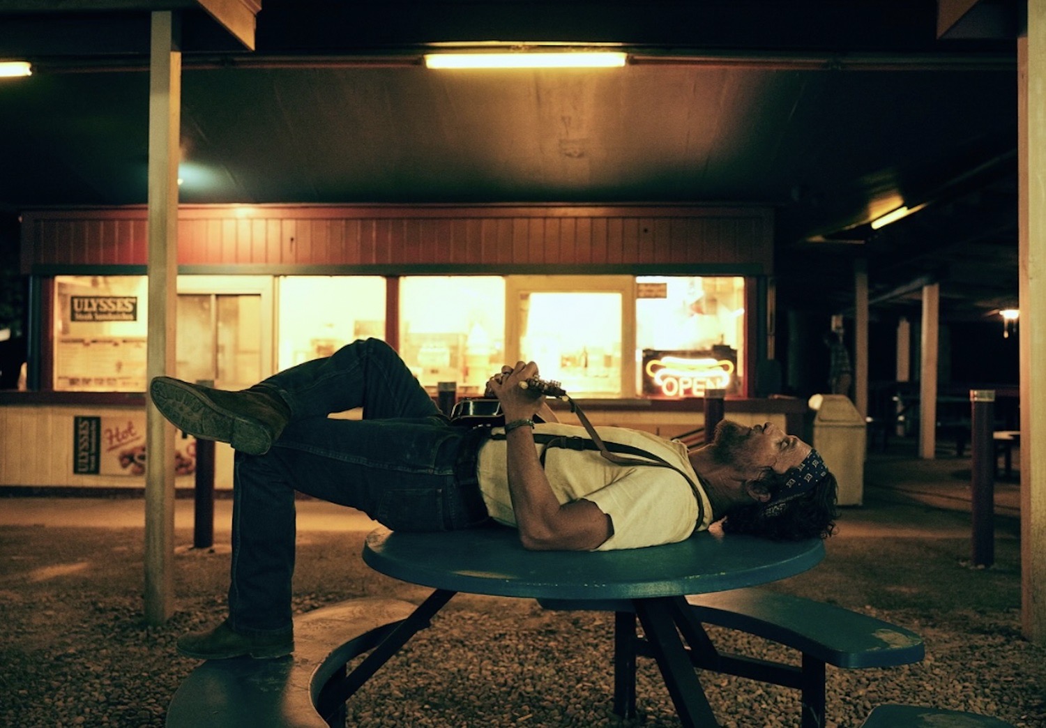 Matthew McConaughey lying on a picnic table with a mandolin outside a lit roadside diner at night, The Rivals of Amziah King